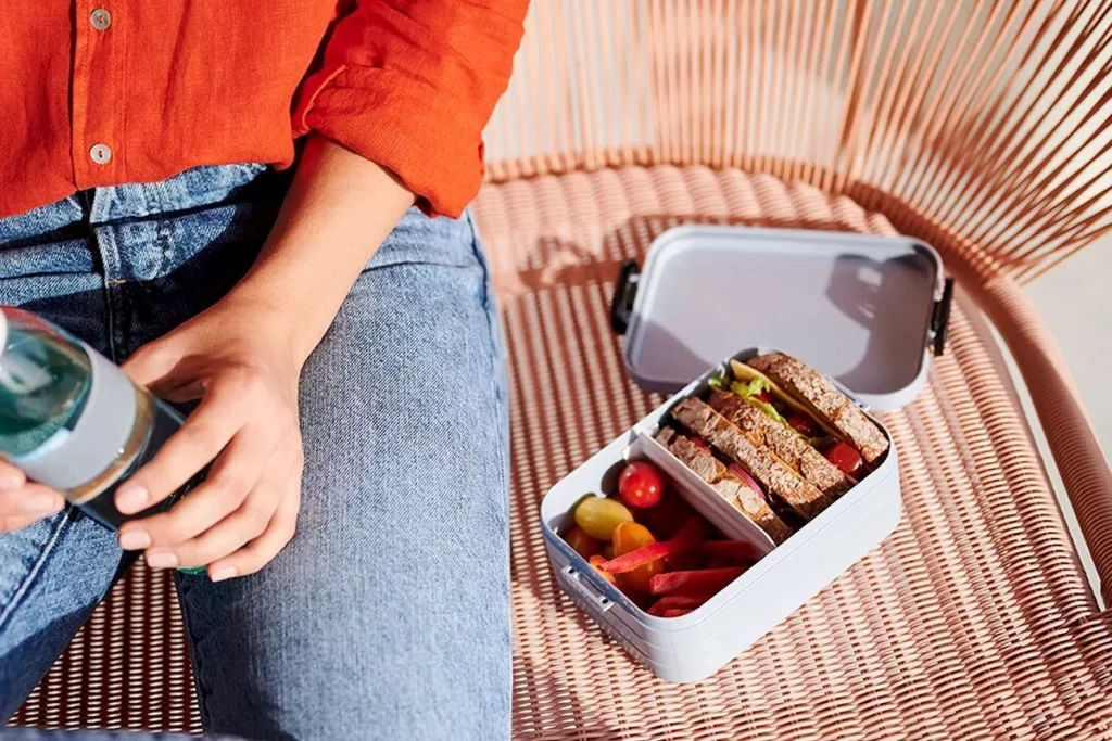 Person mit Lunchbox Vollkornsandwich und Gemüse