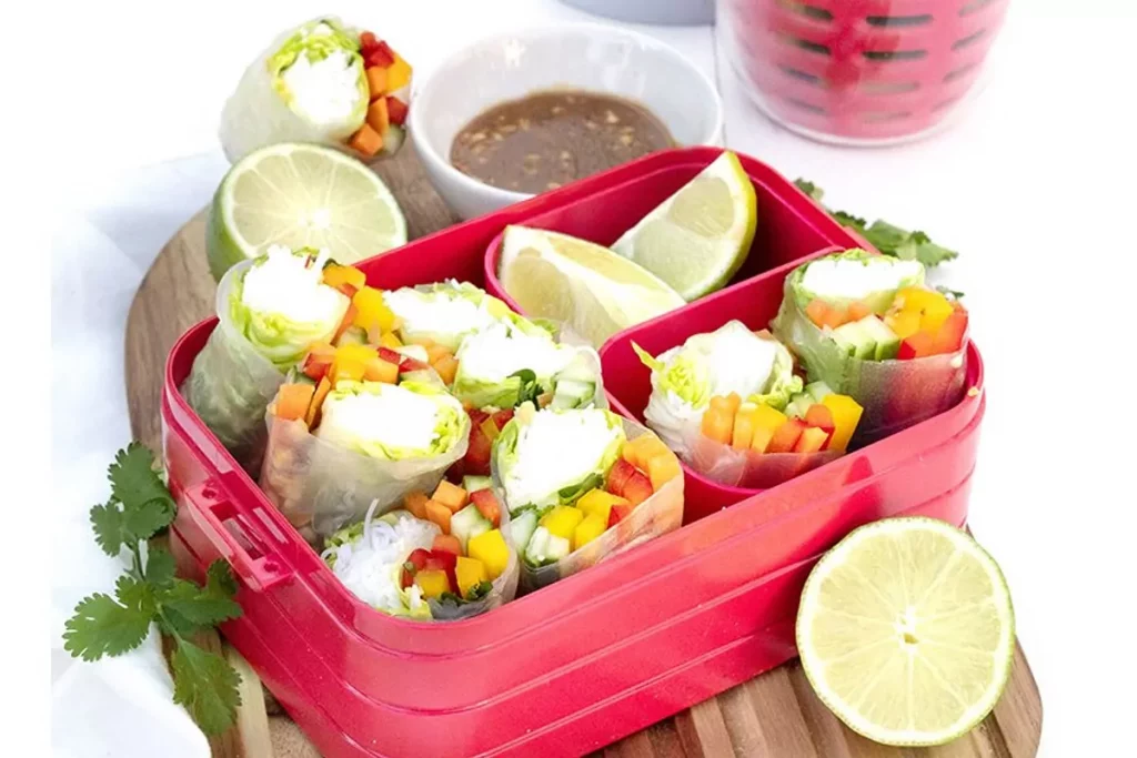 Frühlingsrollen in roter Bento-Lunchbox mit Limetten und Dip